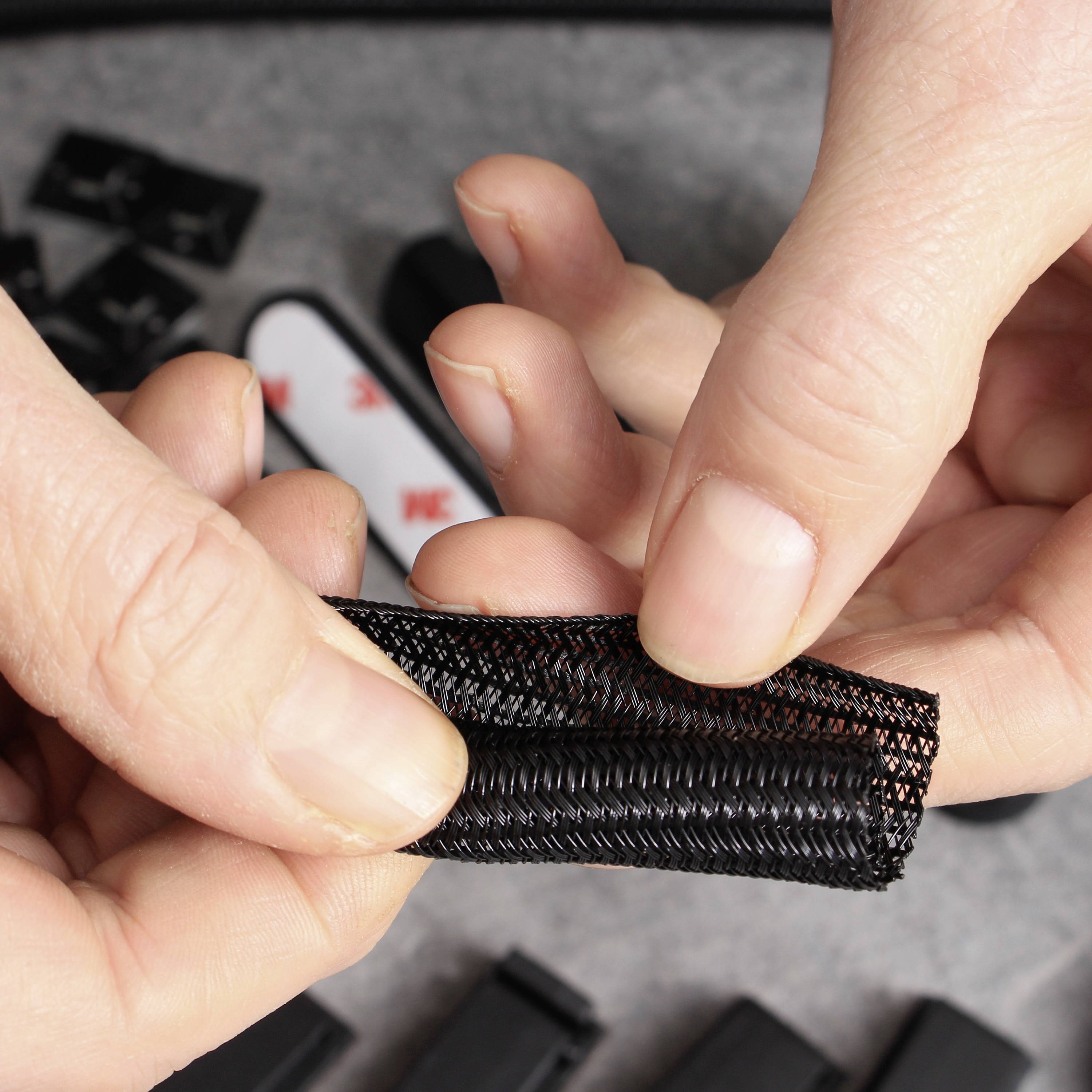 Une personne tient un morceau de fermeture velcro noir à la main. L'environnement montre du matériel de bureau, avec un focus sur la texture et la fonction de la fermeture.