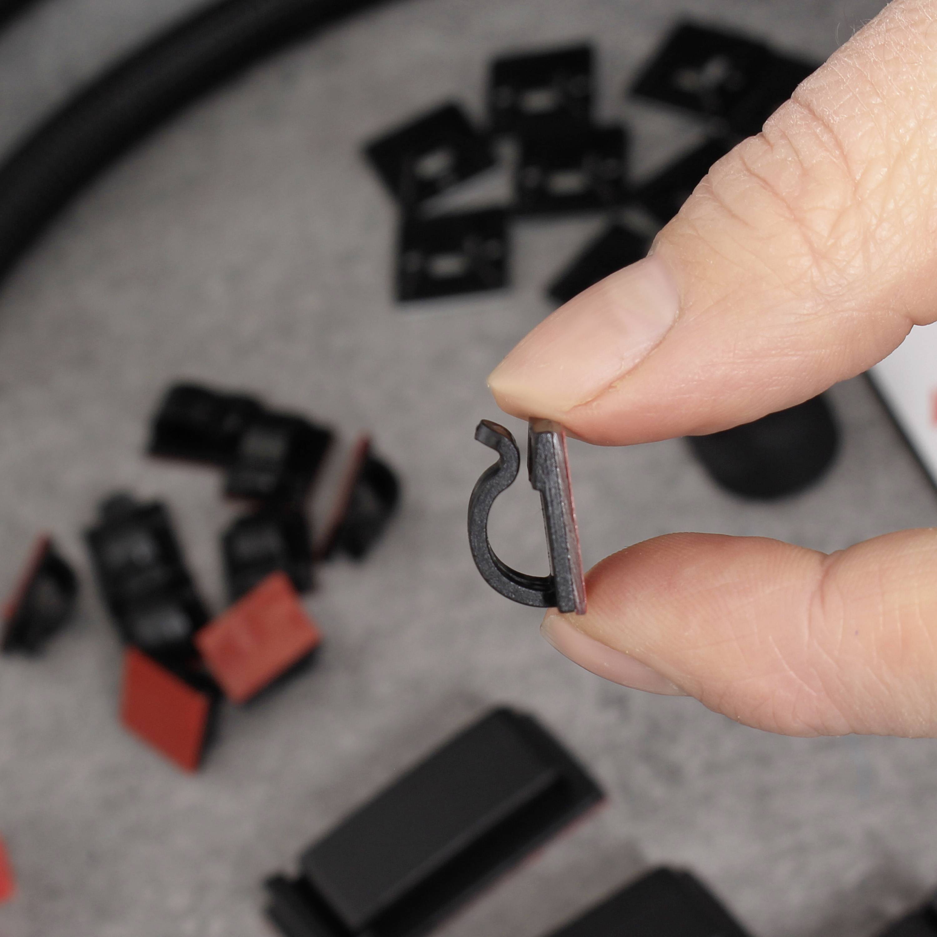 Une main tient une petite pièce en plastique noir, entourée d'autres pièces en plastique, sur un fond gris.