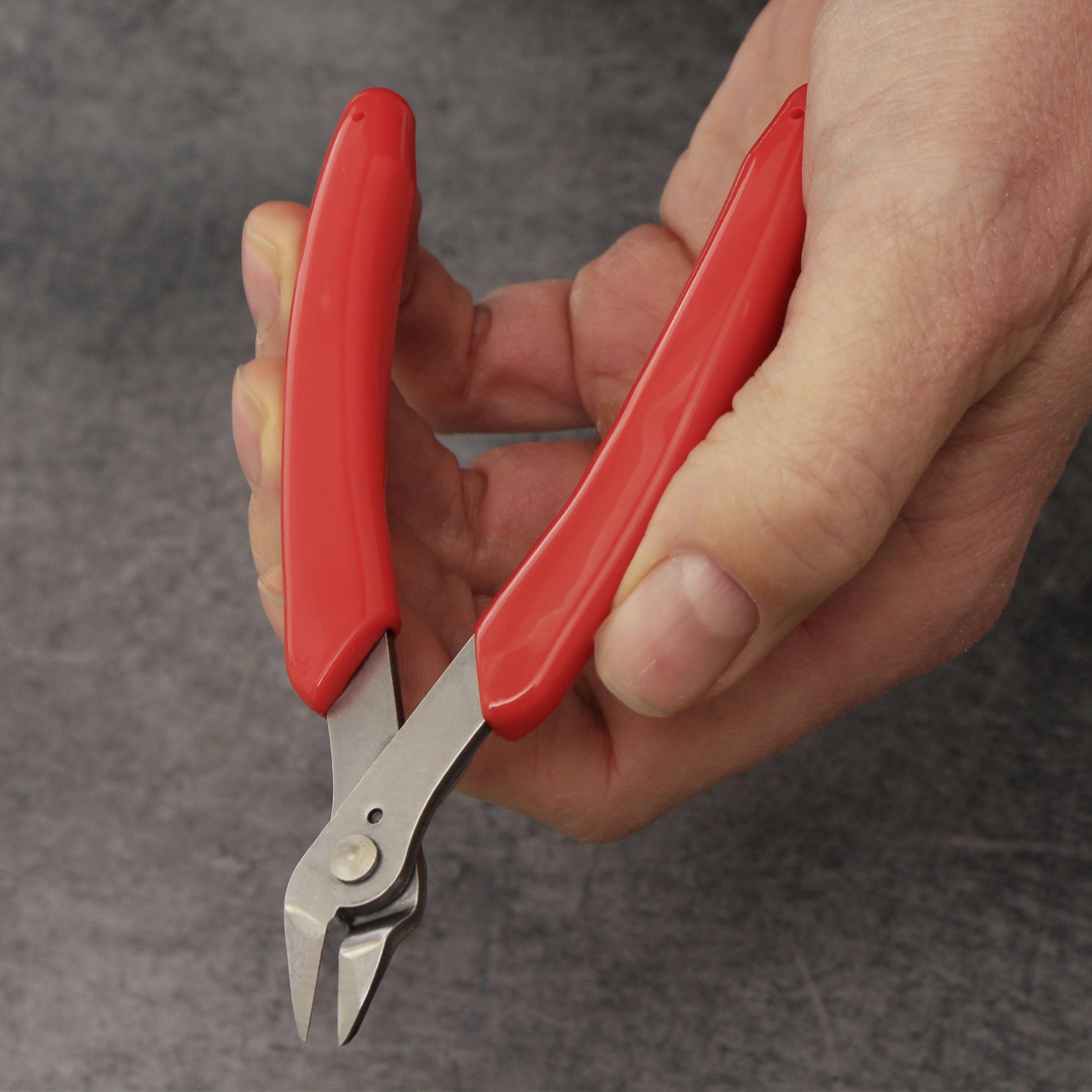 Une main tient un petit coupe-câbles avec des poignées rouges, prêt à couper quelque chose.