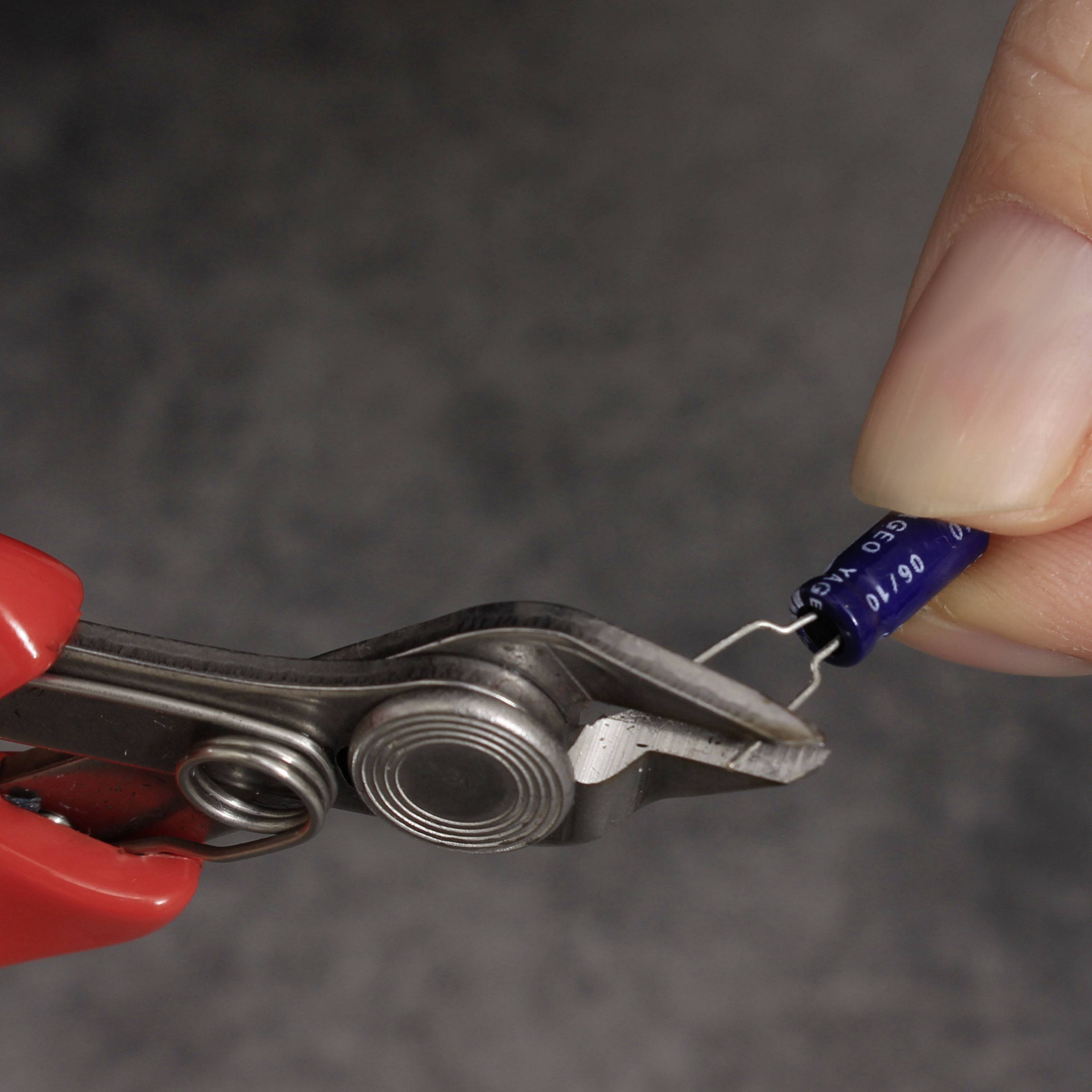 'Une main tient un condensateur bleu relié à une pince crocodile. L'arrière-plan est flou.'