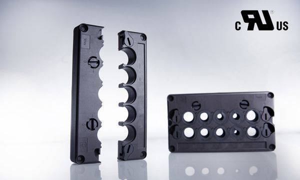Deux pièces en plastique noir rectangulaires avec des ouvertures et des détails gravés. En haut à droite, on peut voir les inscriptions 'c RU us'.