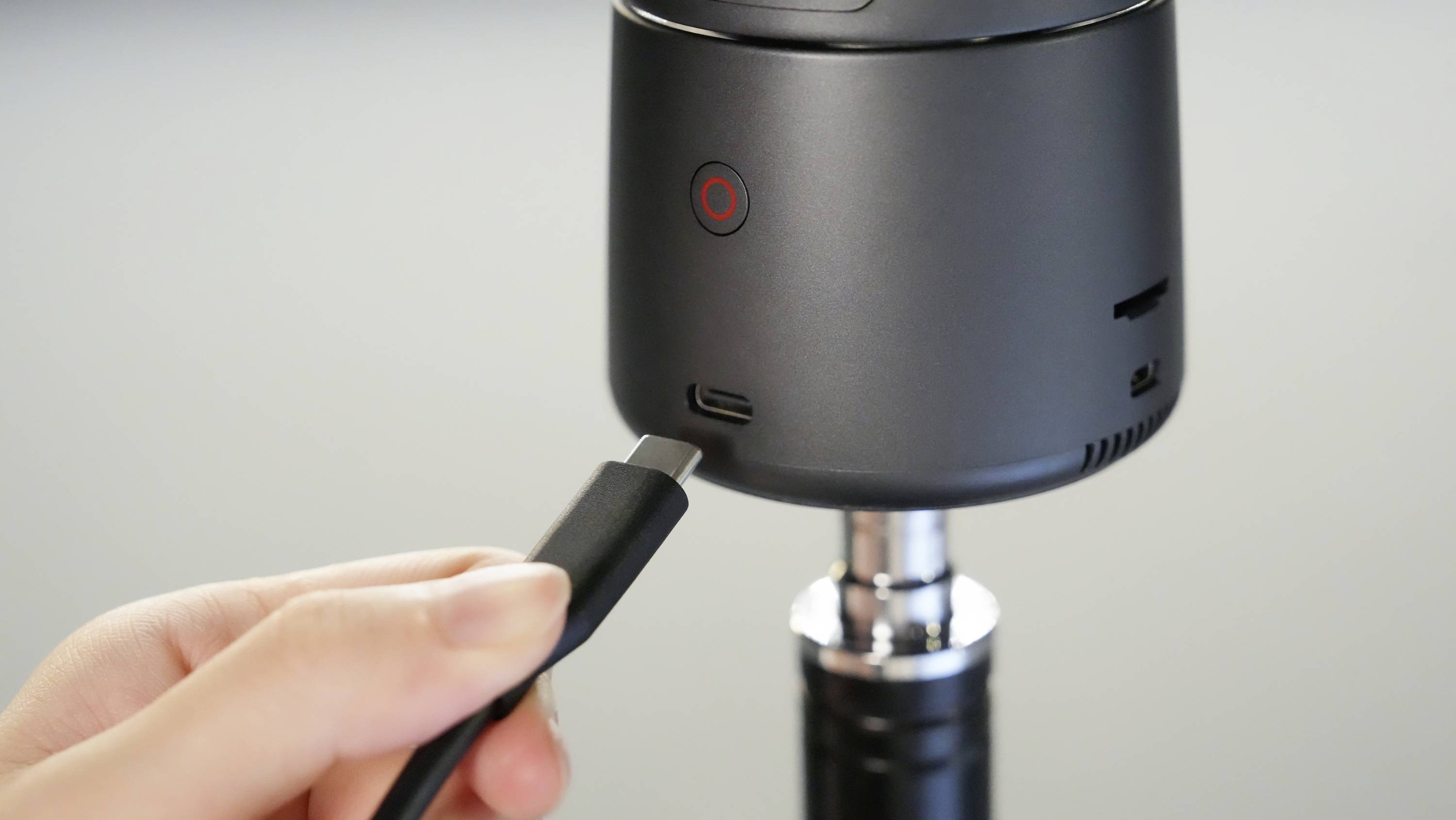 Une main tient un câble USB-C qui est branché dans le port d'un appareil photo noir cylindrique.