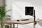 Un bureau moderne avec un écran monté, un clavier et une souris. À côté du bureau se trouve une grande plante verte.