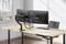 Un bureau équipé de deux écrans montés sur un bras articulé, avec un clavier et une souris. Une chaise est placée à côté.