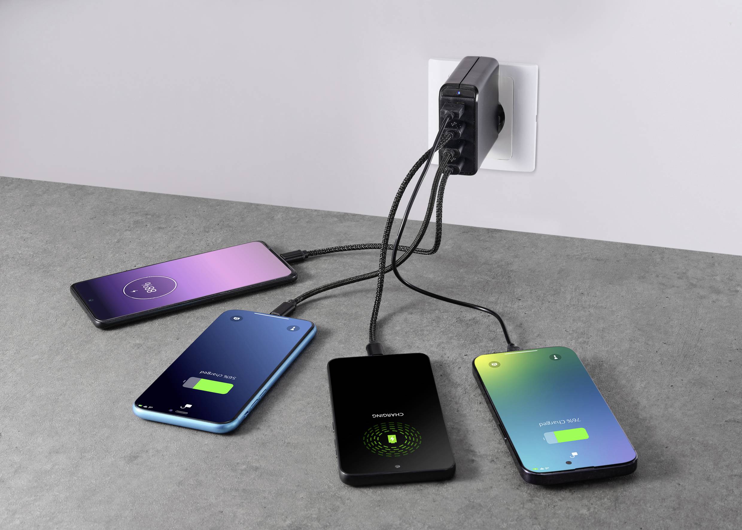Quatre smartphones sont chargés simultanément par un chargeur multiple sur une prise électrique.