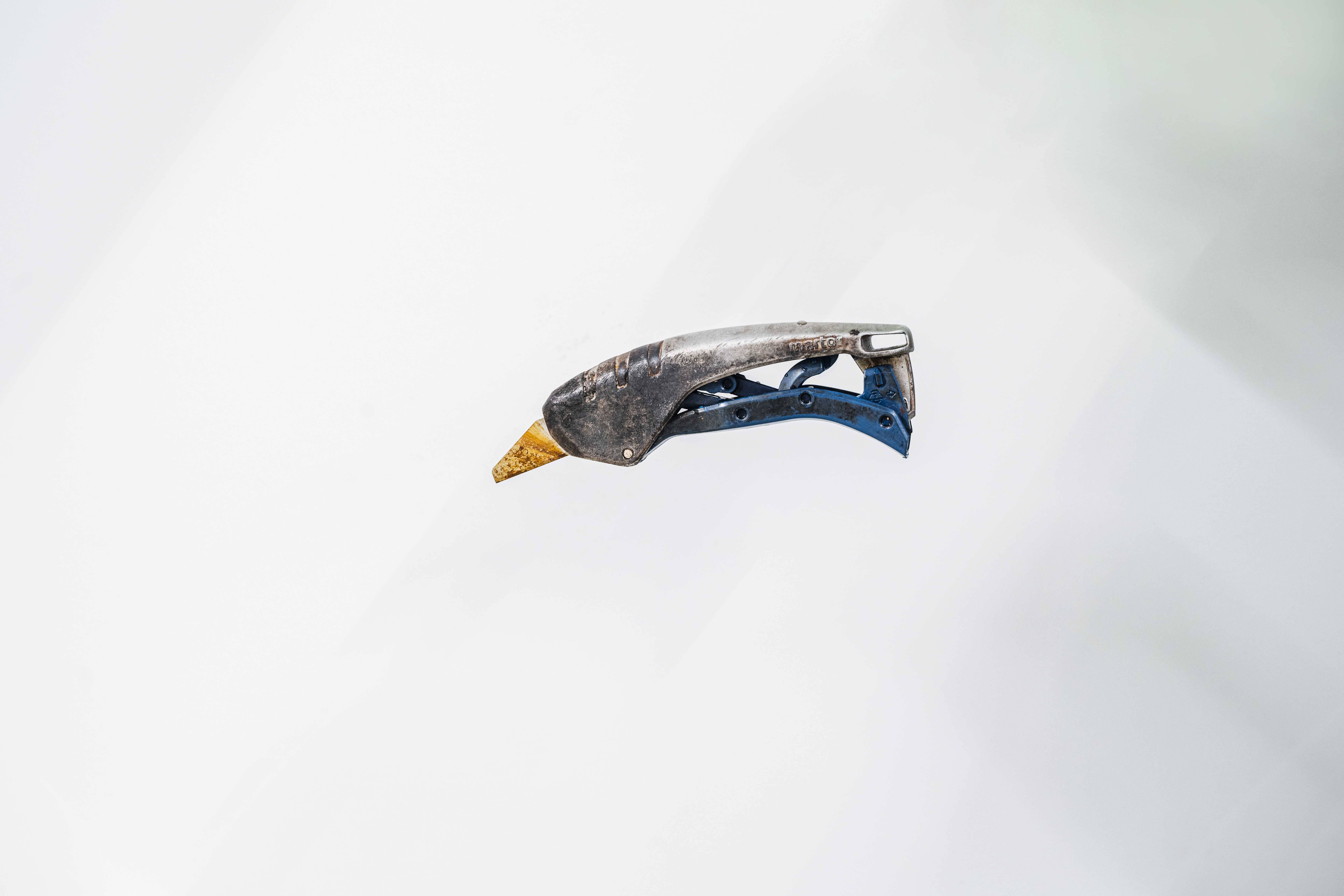 Un vieux outil légèrement rouillé avec une poignée bleue est posé devant un fond blanc. Il s'agit probablement du manche d'un outil de jardinage.