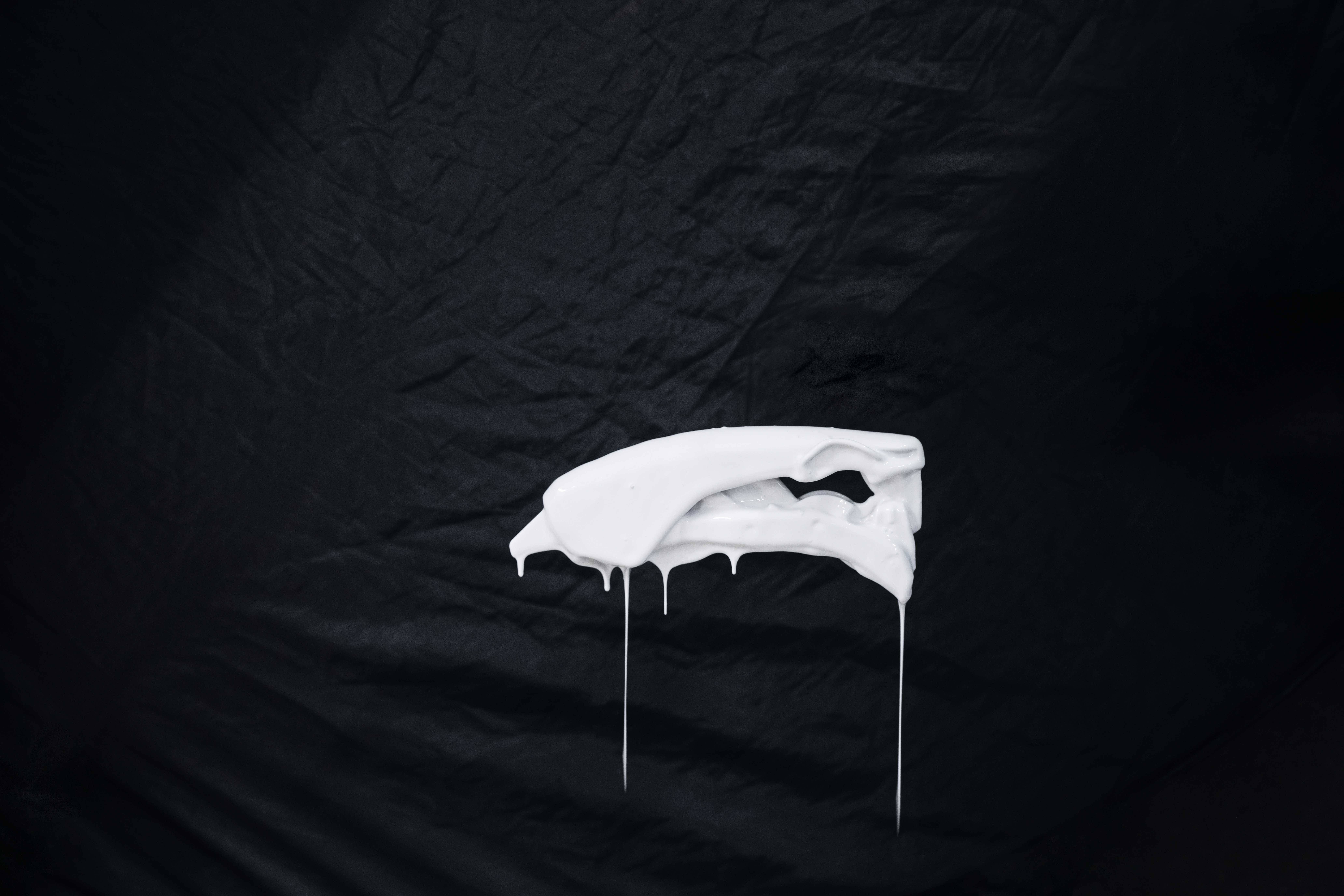 Sculpture abstraite blanche et goutte-à-goutte devant un fond noir.