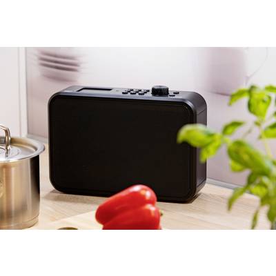 Un poste de radio noir est posé sur un plan de travail de cuisine à côté d'une casserole, de poivrons rouges et de basilic.