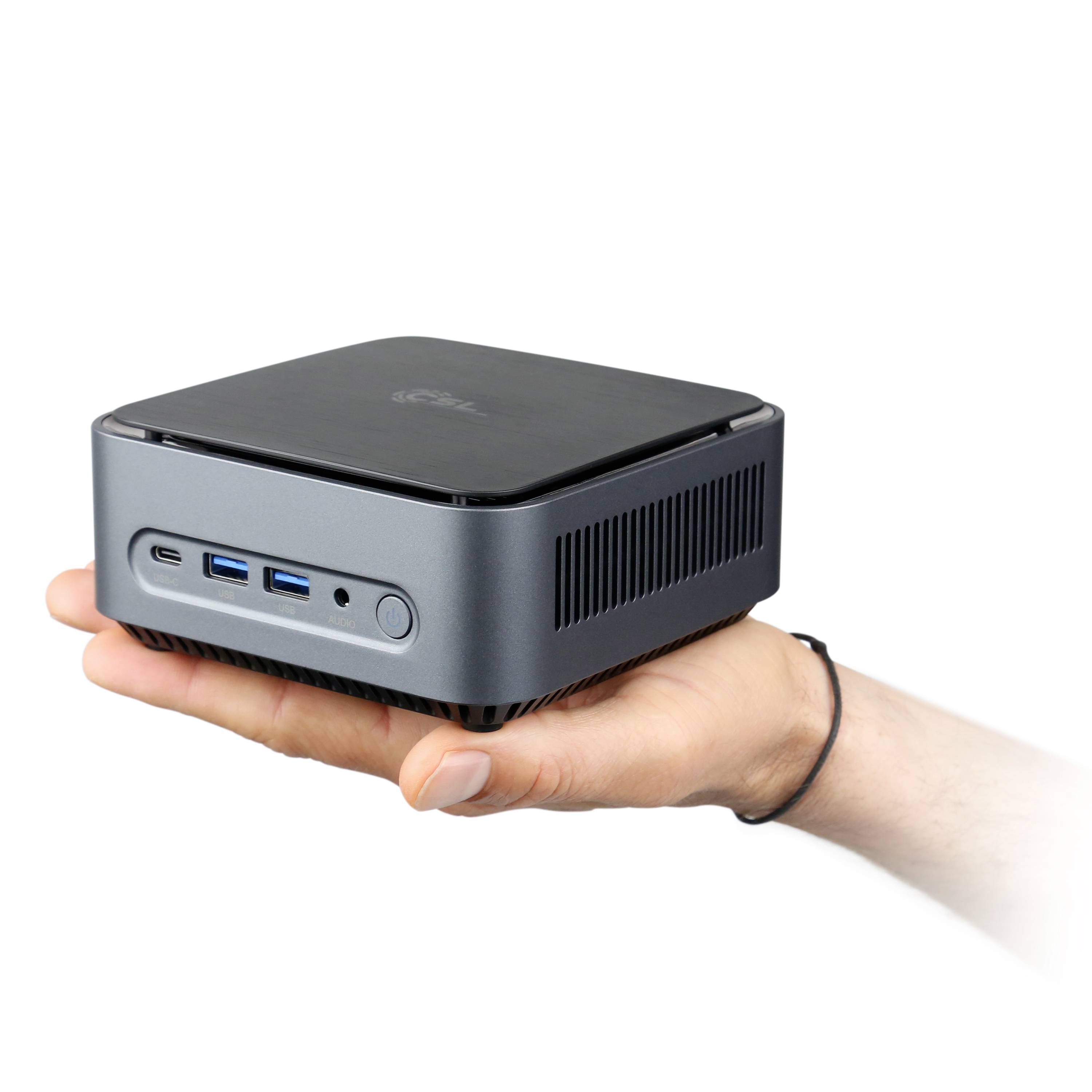 Une main tient un petit ordinateur carré. L'ordinateur possède plusieurs ports à l'avant et un design simple et moderne.