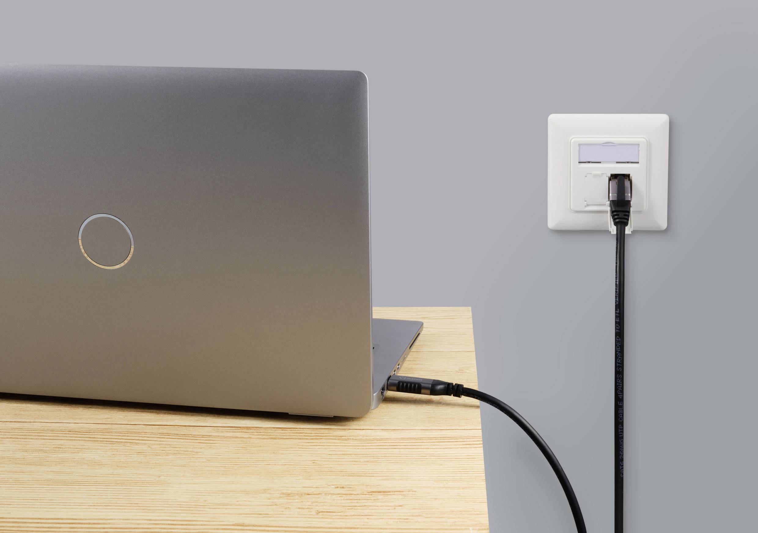 Un ordinateur portable est visible sur une table en bois, connecté à une prise murale par un câble noir.