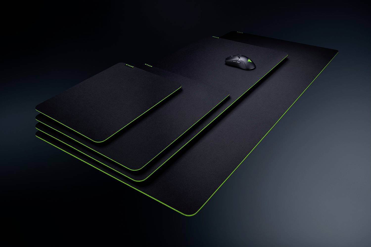 Tapis de souris empilés de différentes tailles, avec une souris gaming posée sur le plus grand pad. Design noir avec bordure verte.