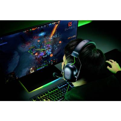 Une personne joue à 'Dota 2' sur un ordinateur, porte un casque audio et se concentre sur l'action colorée et intense qui se déroule à l'écran.
