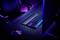 Un setup de gaming avec un clavier rétroéclairé, une souris gaming et un écran sur un bureau, baigné dans une ambiance lumineuse violette.