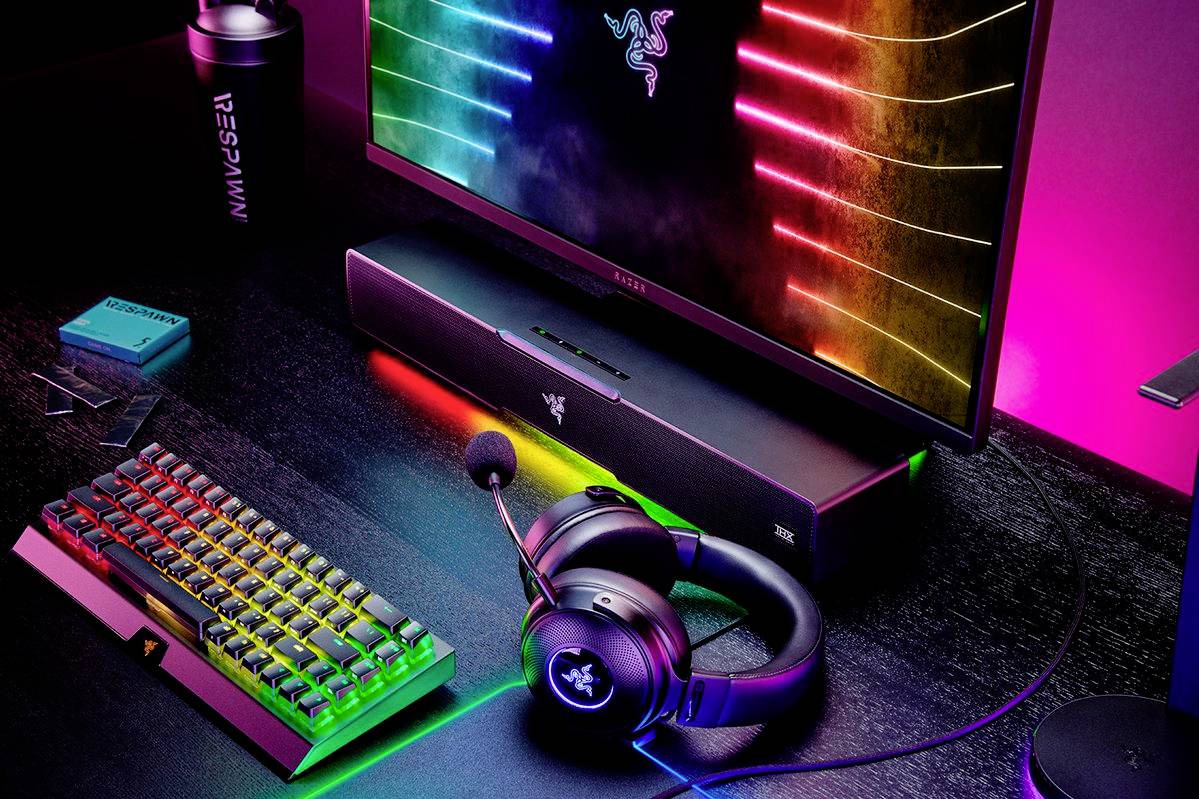 Configuration de jeu avec un clavier rétroéclairé, un moniteur, des enceintes et un casque audio. Les lumières brillent dans des couleurs arc-en-ciel et créent une atmosphère futuriste.