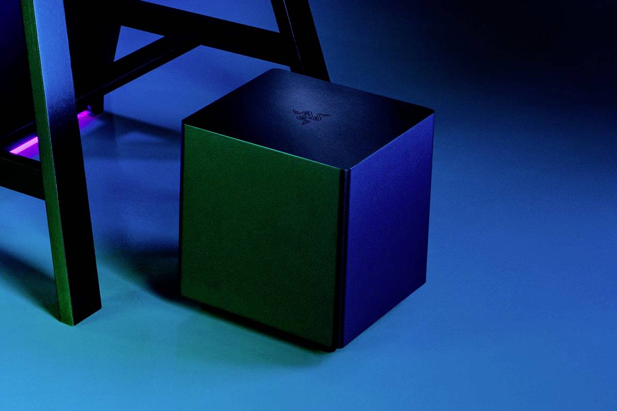 Un haut-parleur noir cubique sur un sol bleu, à côté d'une partie d'une chaise, dans une lumière sombre et atmosphérique.