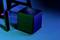Un haut-parleur noir cubique sur un sol bleu, à côté d'une partie d'une chaise, dans une lumière sombre et atmosphérique.