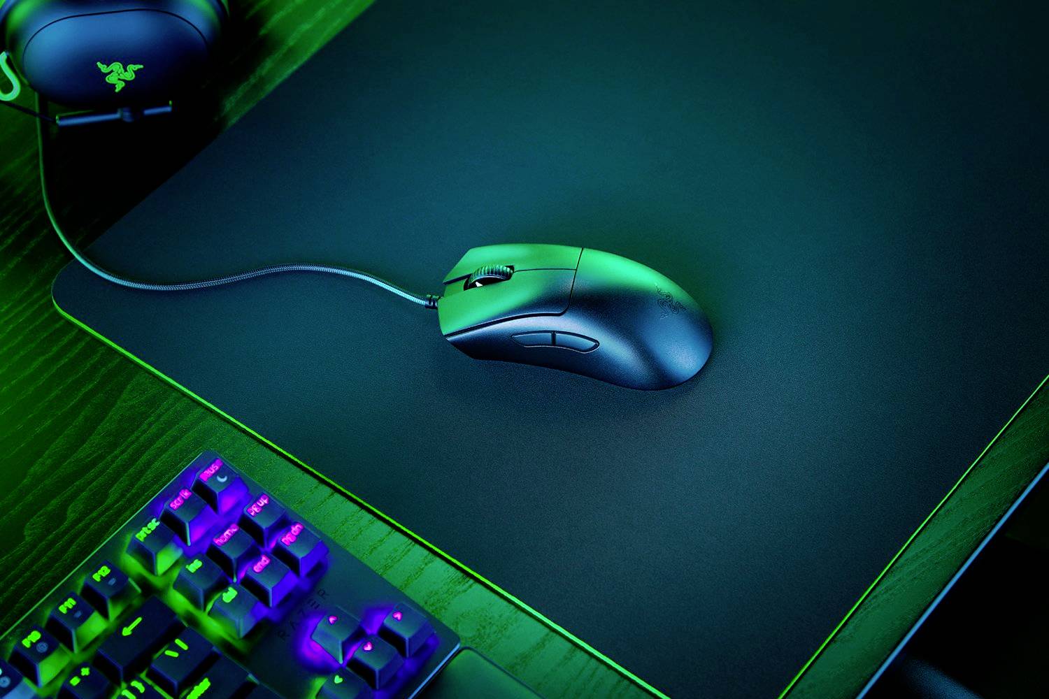 Une souris d'ordinateur filaire repose sur un tapis de souris lumineux, à côté d'un clavier partiellement visible et des écouteurs.