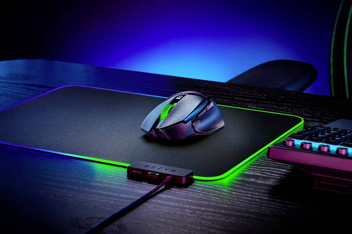 Une souris gaming repose sur un tapis de souris rétroéclairé sur un bureau, à côté d'un clavier ; le tout baigné dans une lumière bleu-vert.