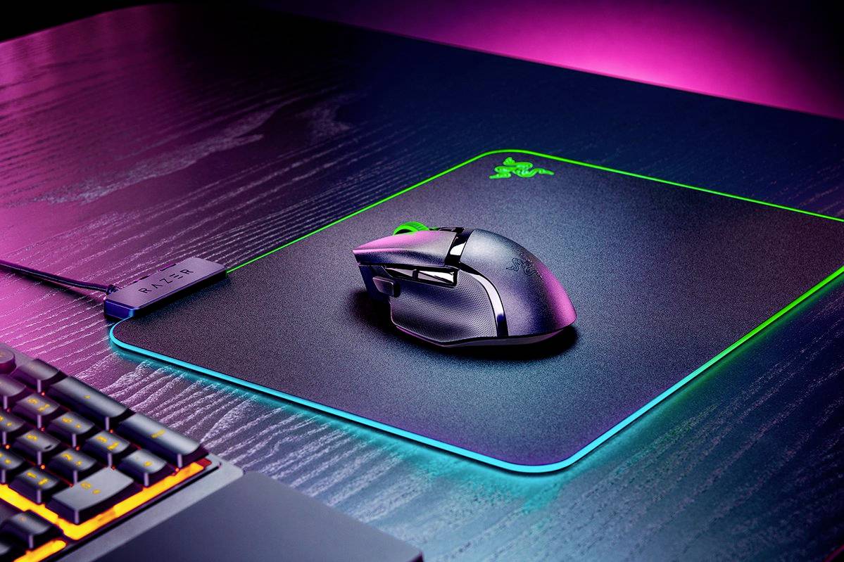 Une souris et un clavier de gaming sur un bureau illuminé aux couleurs néon. La souris est posée sur un tapis de souris à bordure lumineuse.