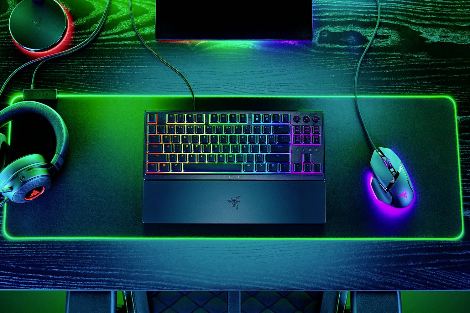 Configuration de jeu avec un clavier et une souris à éclairage RVB sur un tapis de souris lumineux. Un casque est posé à côté sur le bureau.