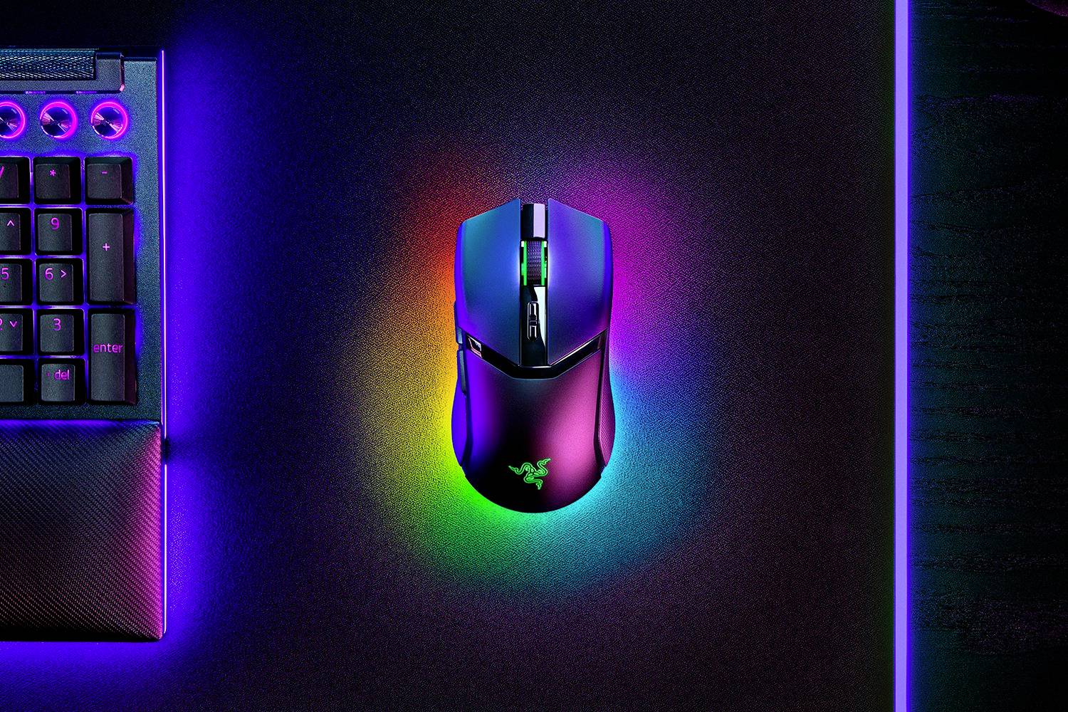 Une souris de jeu sans fil avec des lumières LED colorées est posée sur un bureau éclairé à côté d'un clavier.
