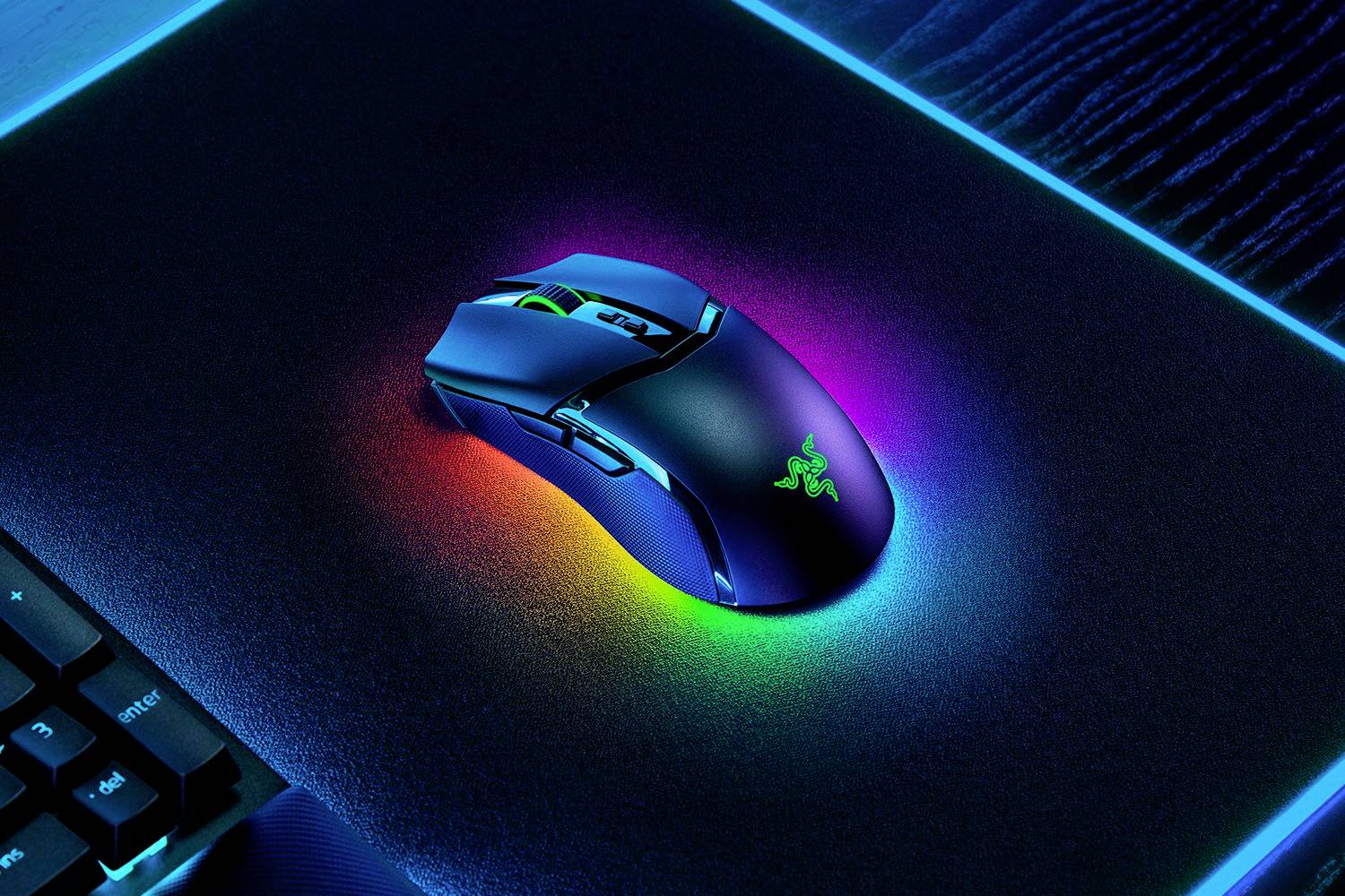 Une souris de gaming noire avec des couleurs RVB lumineuses est posée sur un tapis de souris éclairé, à côté d'un clavier, sur une table sombre.