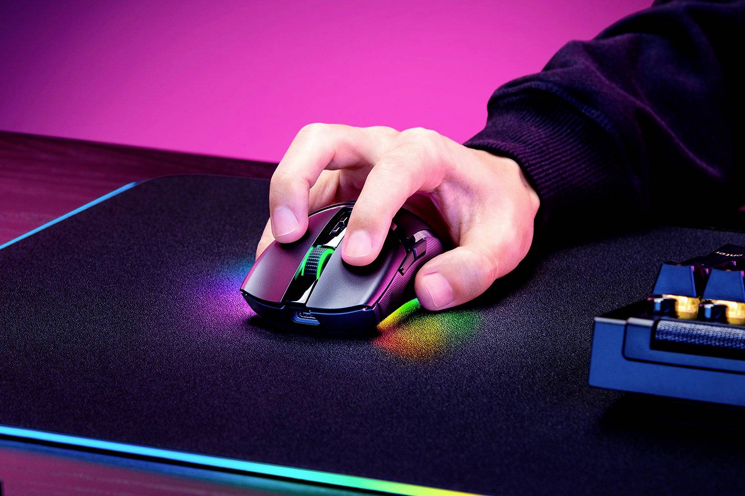 Une main tient une souris gaming avec un éclairage multicolore sur un tapis de souris. Des couleurs vives illuminent l'arrière-plan.