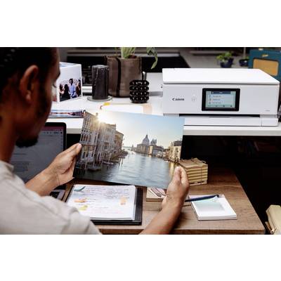 Une personne regarde une photo de Venise, tout juste imprimée sur un imprimante posée sur un bureau. Des plantes et du matériel de bureau sont visibles en arrière-plan.