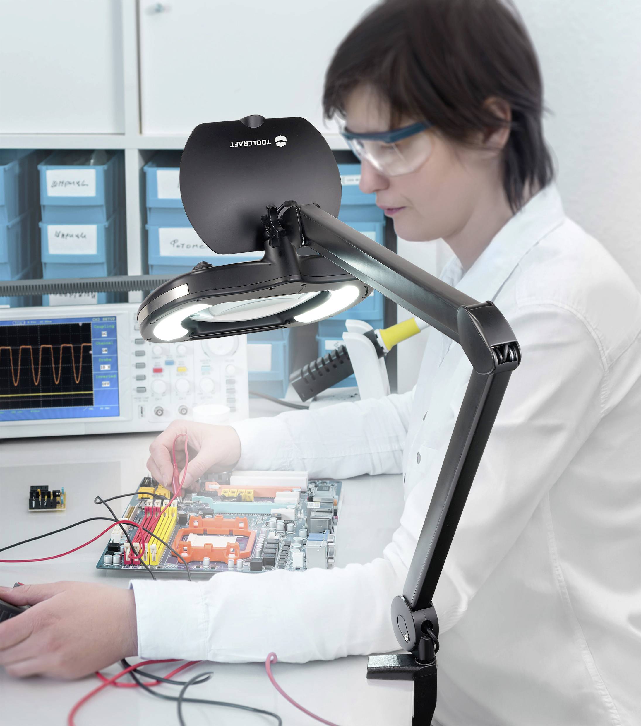 Une personne travaille de manière concentrée sur un circuit avec des câbles et des cartes électroniques, entourée d'appareils techniques et d'un oscilloscope.