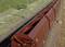 Train de marchandises avec des wagons bruns roulant sur une voie ferrée. L'environnement est composé d'herbe et d'une clôture électrique. Photographié en plongée oblique.