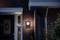 Une maison éclairée avec une façade en briques la nuit. Une lampe projette de la lumière sur le mur à côté d'une porte d'entrée noire.