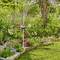 Un jardin avec des plantes en fleurs et un arroseur qui répand de l'eau pour irriguer la végétation. Une pelouse bien entretenue est visible.
