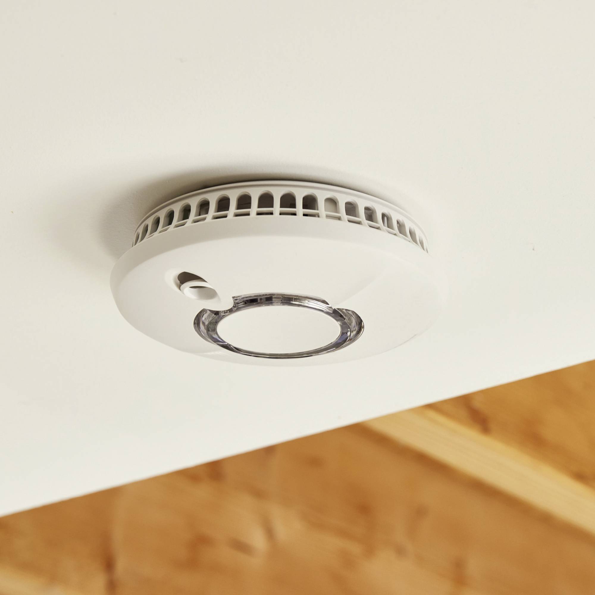 Détecteur de fumée sur un plafond blanc montrant son installation dans une pièce avec des poutres en bois. Fonction principale : alerter en cas de développement de fumée.