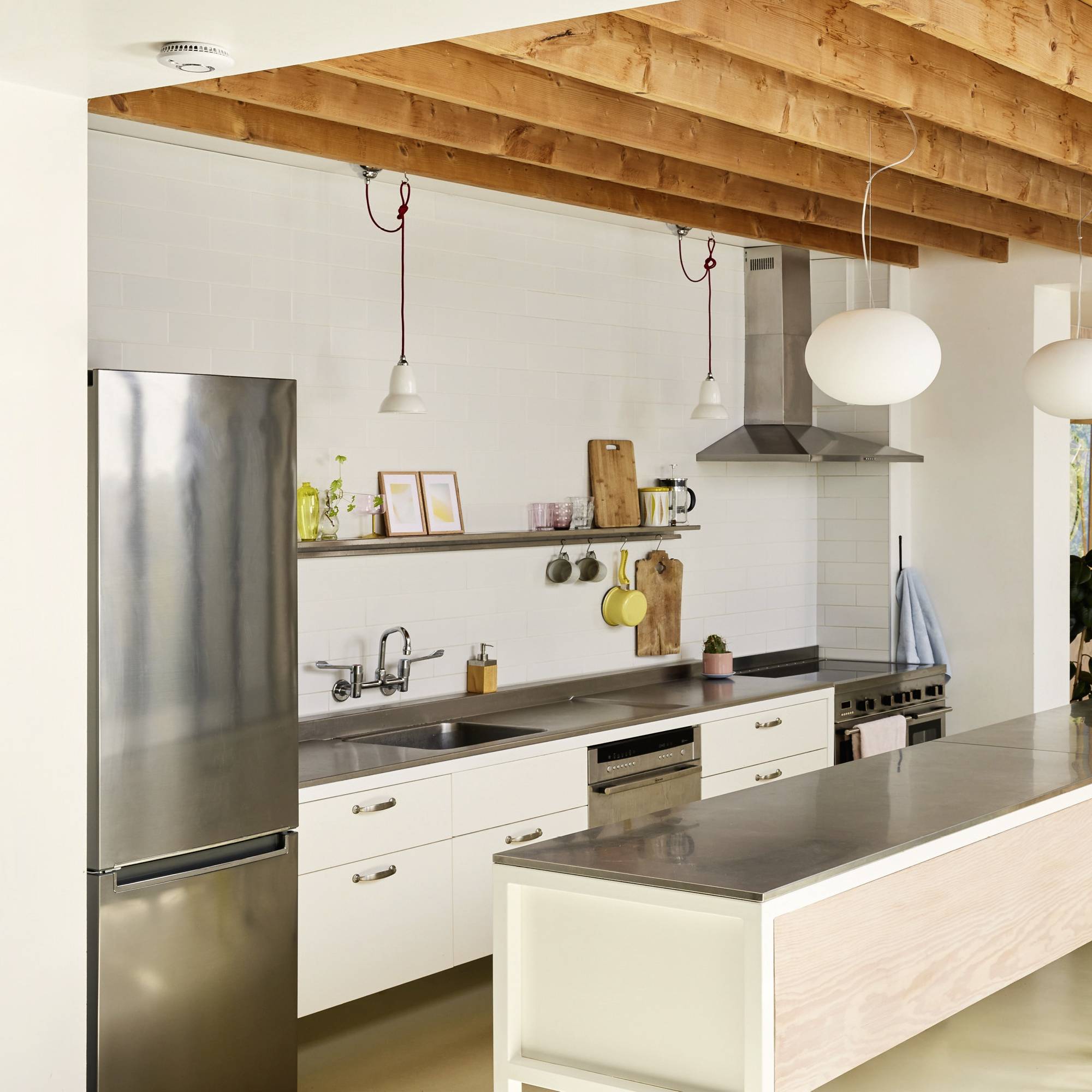 Cuisine moderne avec plafond à poutres apparentes en bois, étagère design au-dessus de l'évier, appareils en acier inoxydable et grand îlot central avec plan de travail.