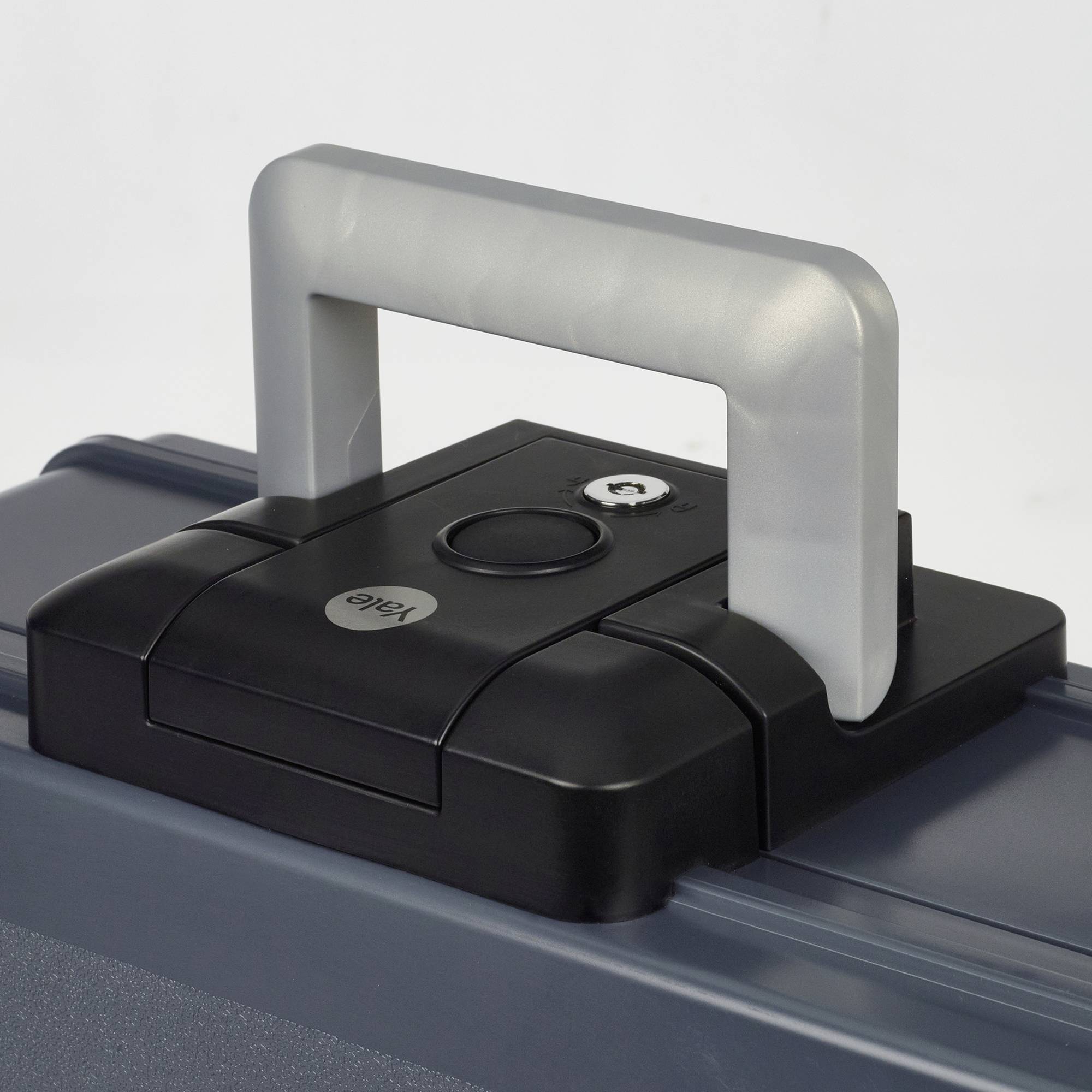 Poignée noire pour valise avec trou de serrure et logo rond sur une valise grise.