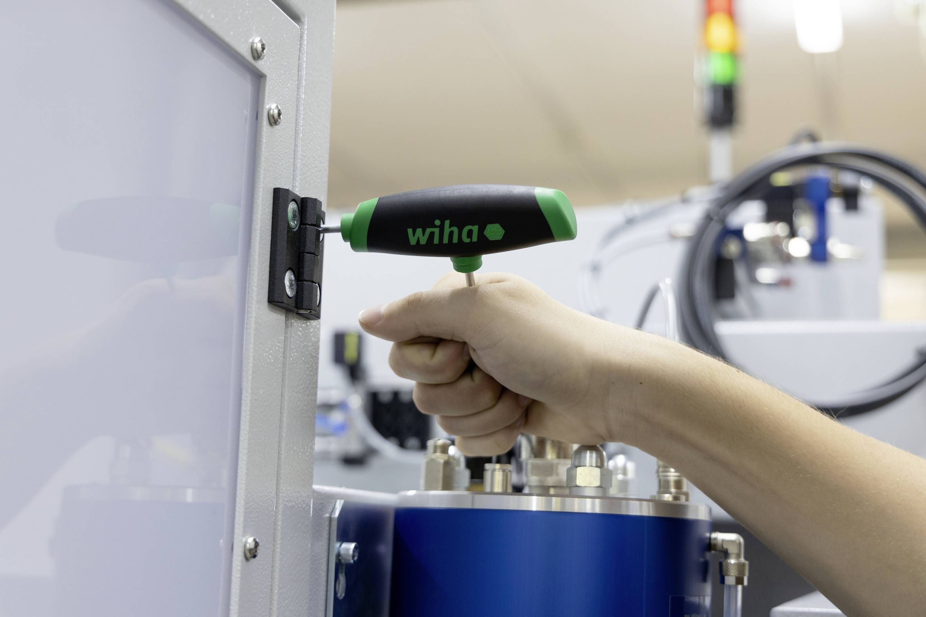 Une main utilise un tournevis à poignée en T pour serrer une vis sur une porte métallique. La porte appartient à une machine.