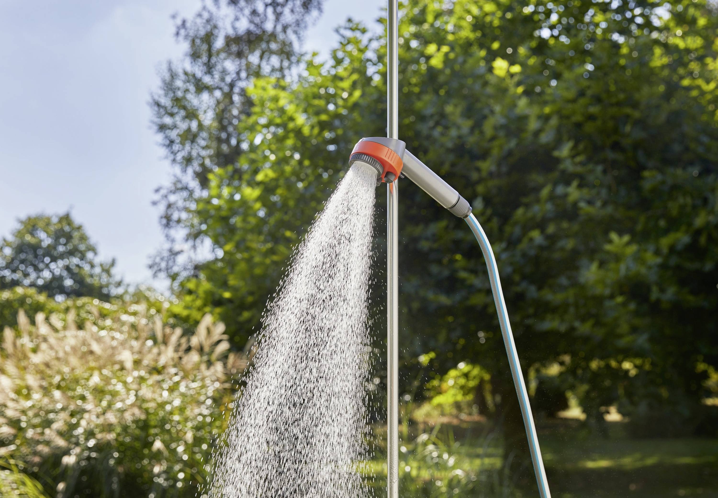 Douche extérieure avec eau coulante, entourée de verdure, sous un ciel dégagé