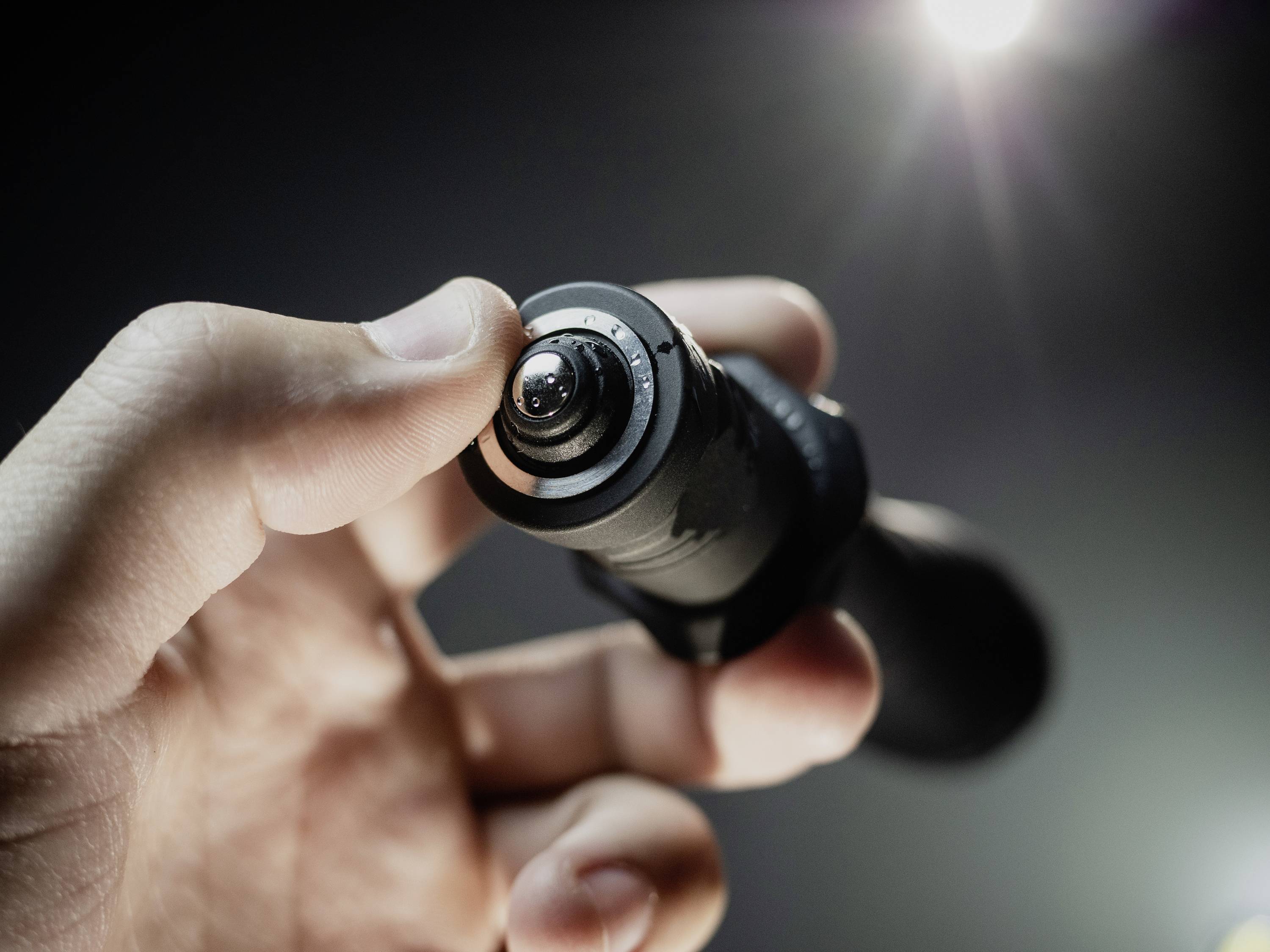 Une main tient un petit objet cylindrique avec une lentille, probablement un appareil photo ou un objectif, dans une faible lumière.