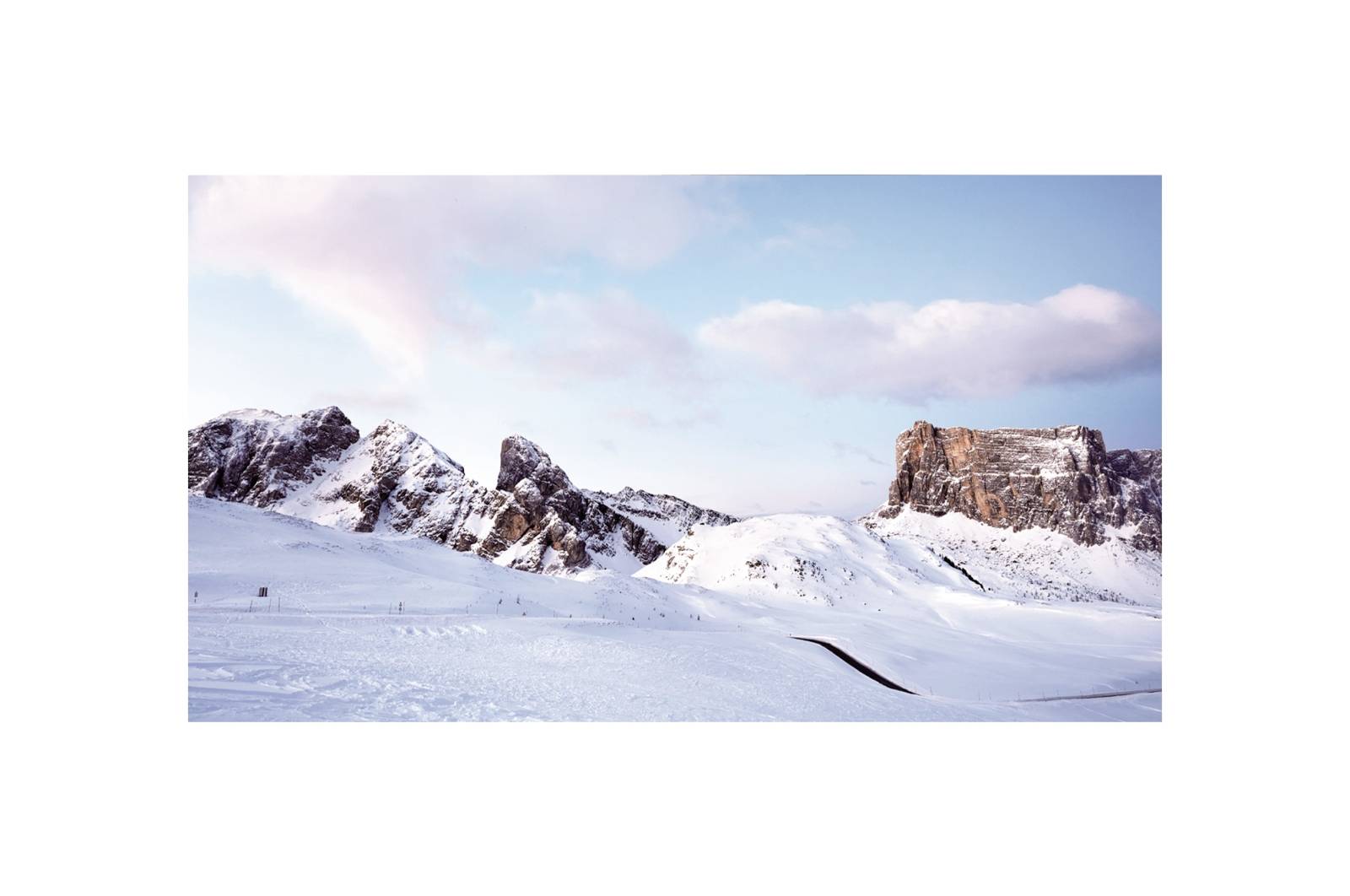 Paysage montagneux enneigé sous un ciel bleu parsemé de quelques nuages. Sommets majestueux en arrière-plan, vaste étendue enneigée ouverte au premier plan.
