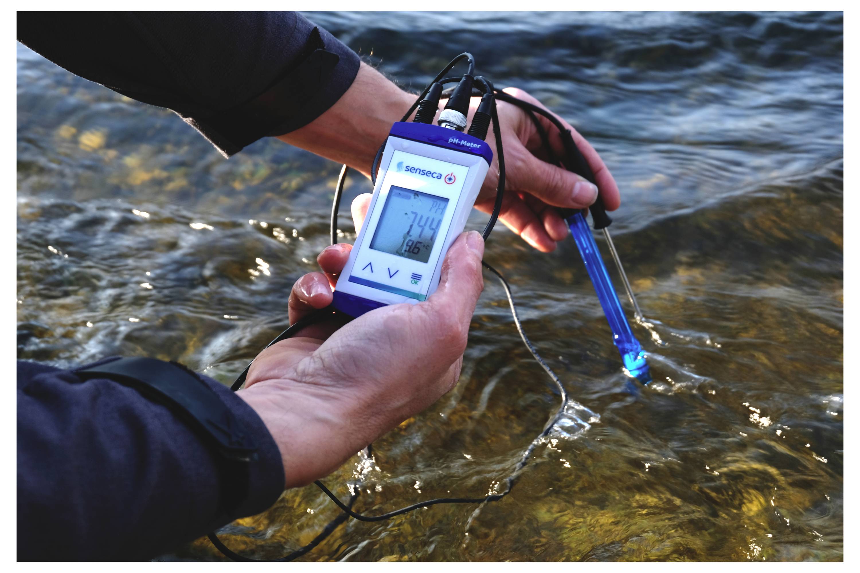 Une personne utilisant un appareil numérique pour mesurer la qualité de l'eau d'une rivière, affichant une lecture de 7,4.