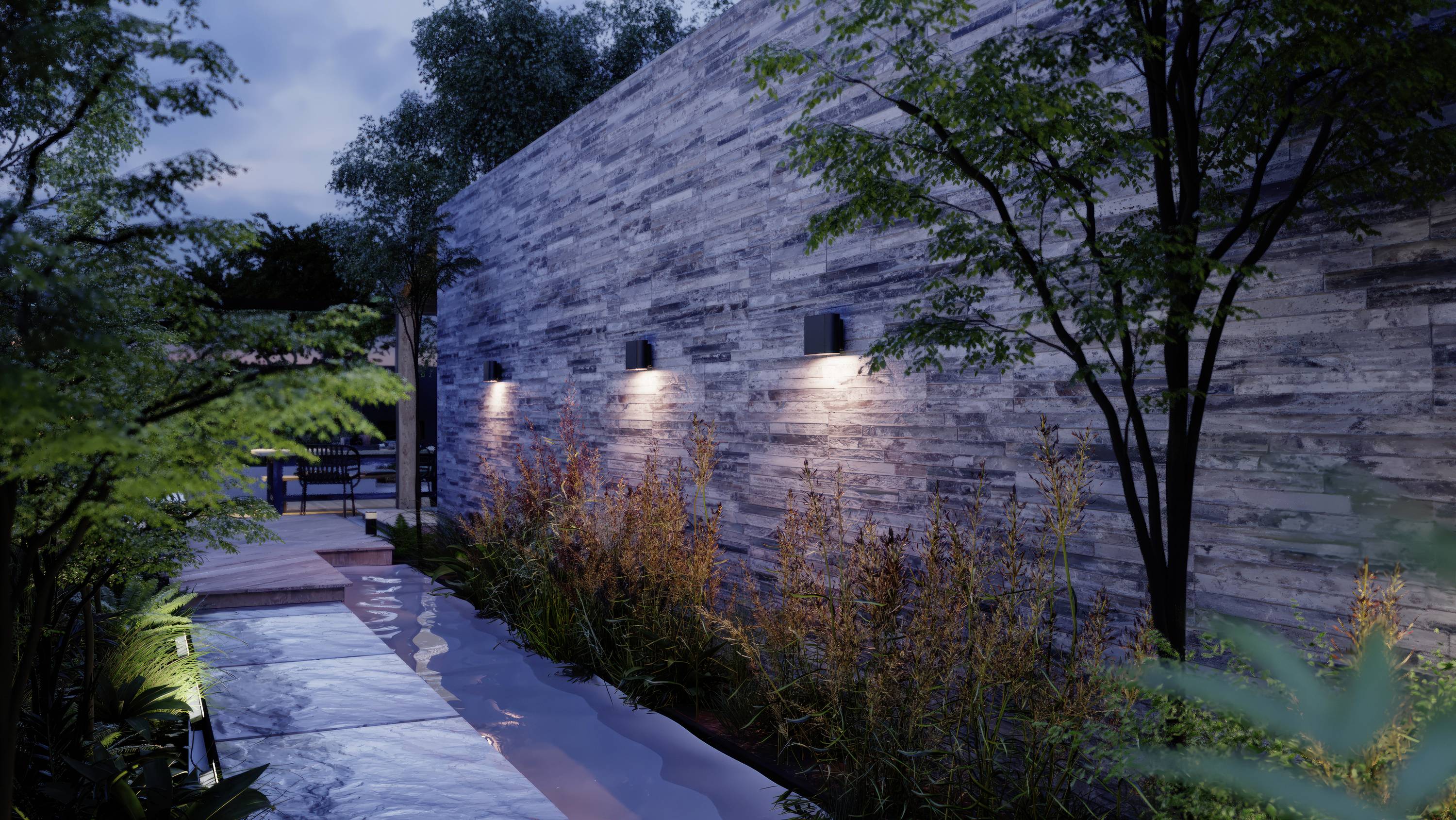 Chemin bordé d'un élément d'eau et d'arbres le long d'un mur de pierre éclairé dans un jardin moderne au crépuscule.