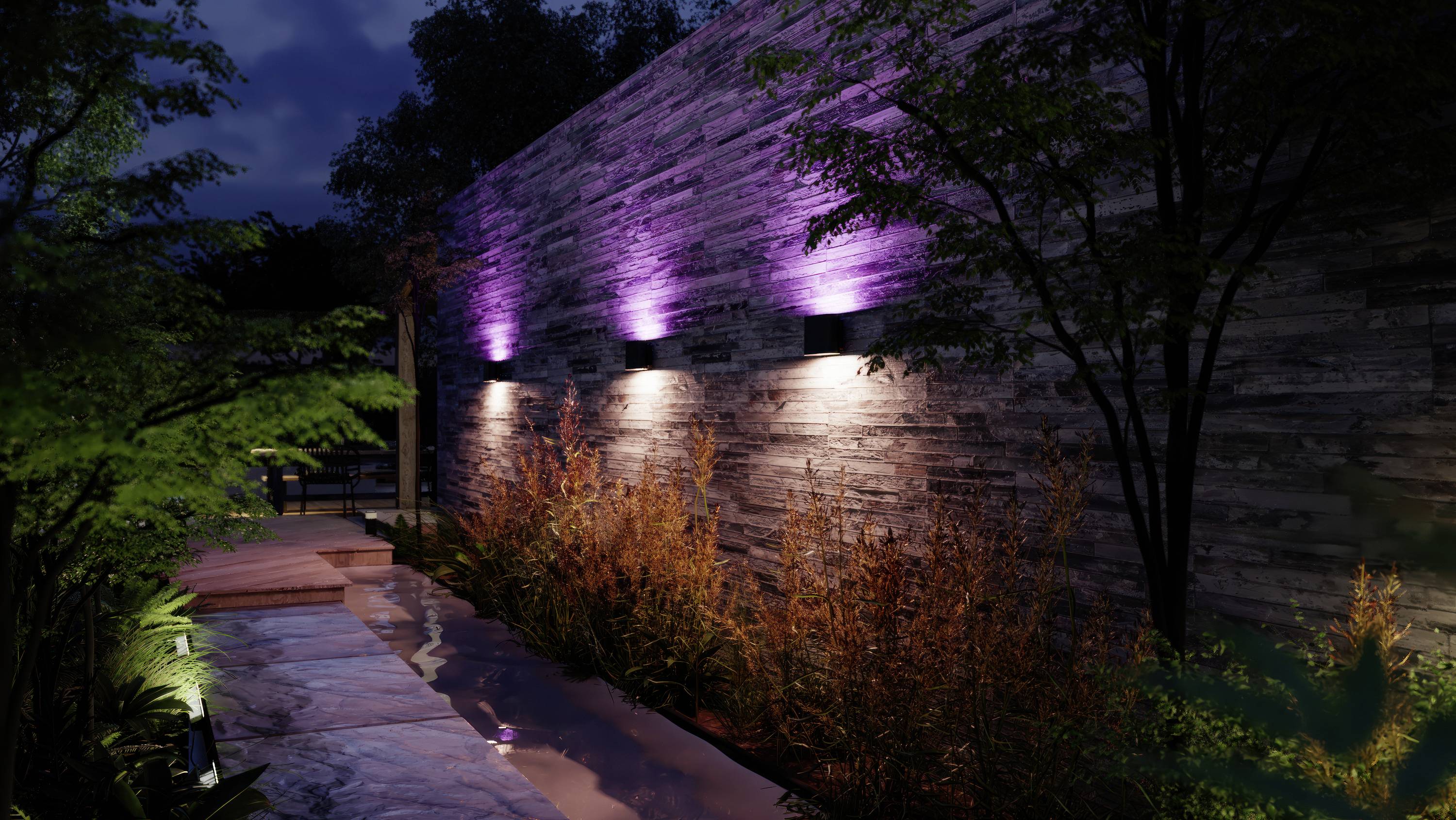 Chemin de jardin la nuit avec un mur de pierre éclairé en lilas, bordé d'arbres et de plantes qui créent une atmosphère paisible et atmosphérique.