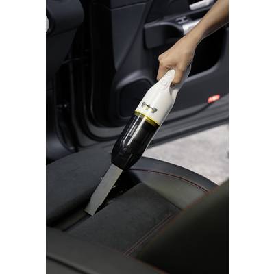 Une main utilise un petit aspirateur portable pour enlever la saleté entre les sièges d'une voiture.