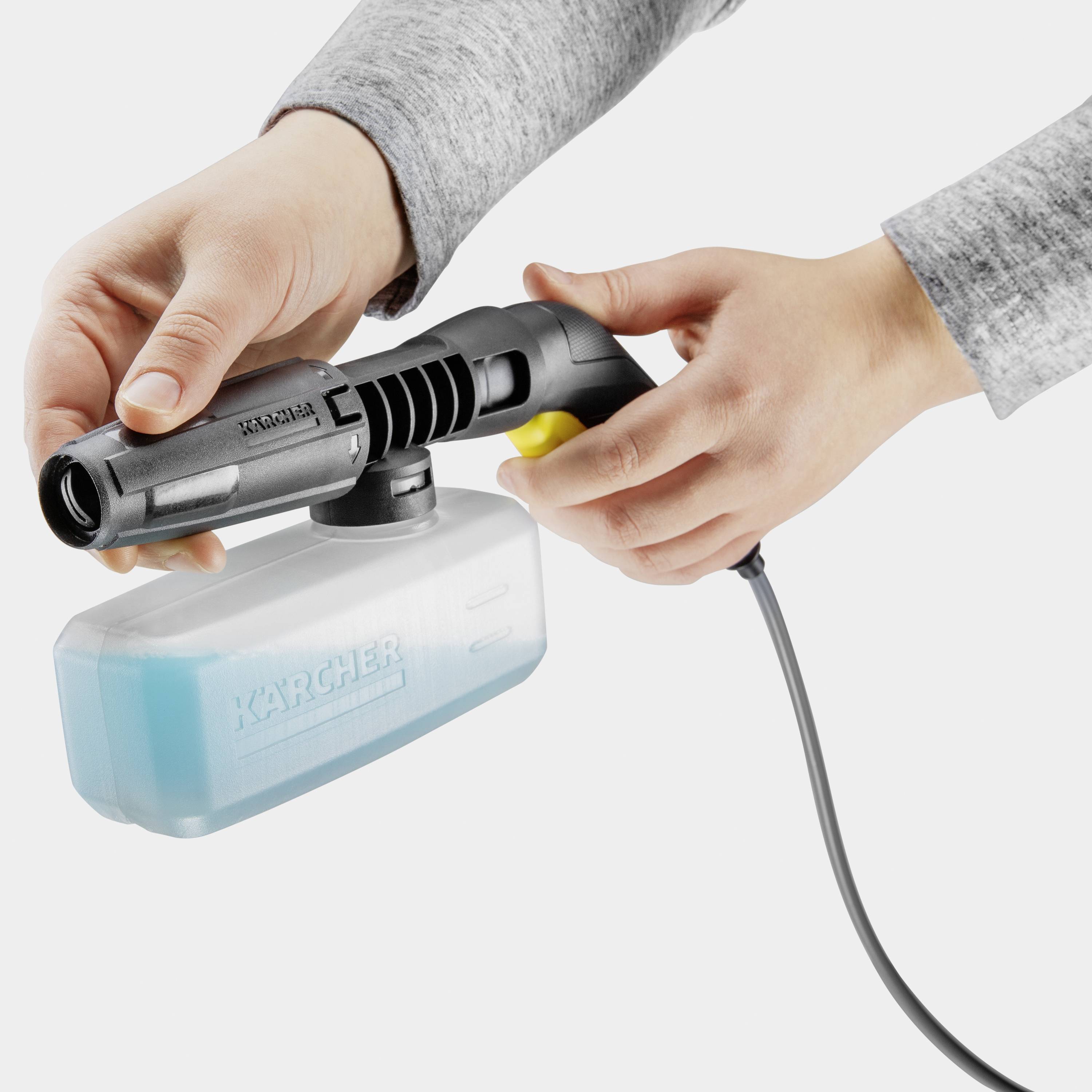 Une personne tient une buse de nettoyage avec un récipient bleu de liquide. Outil de Kärcher avec câble d'alimentation électrique.