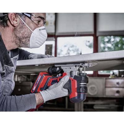 Un homme portant un équipement de protection utilise une scie sauteuse rouge pour couper une feuille de matériau dans un environnement d'atelier.