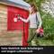 Une personne peint un mur en bois en rouge avec un pistolet à peinture. Texte : 'Grande mobilité grâce à la bandoulière et au long tuyau d'air'.