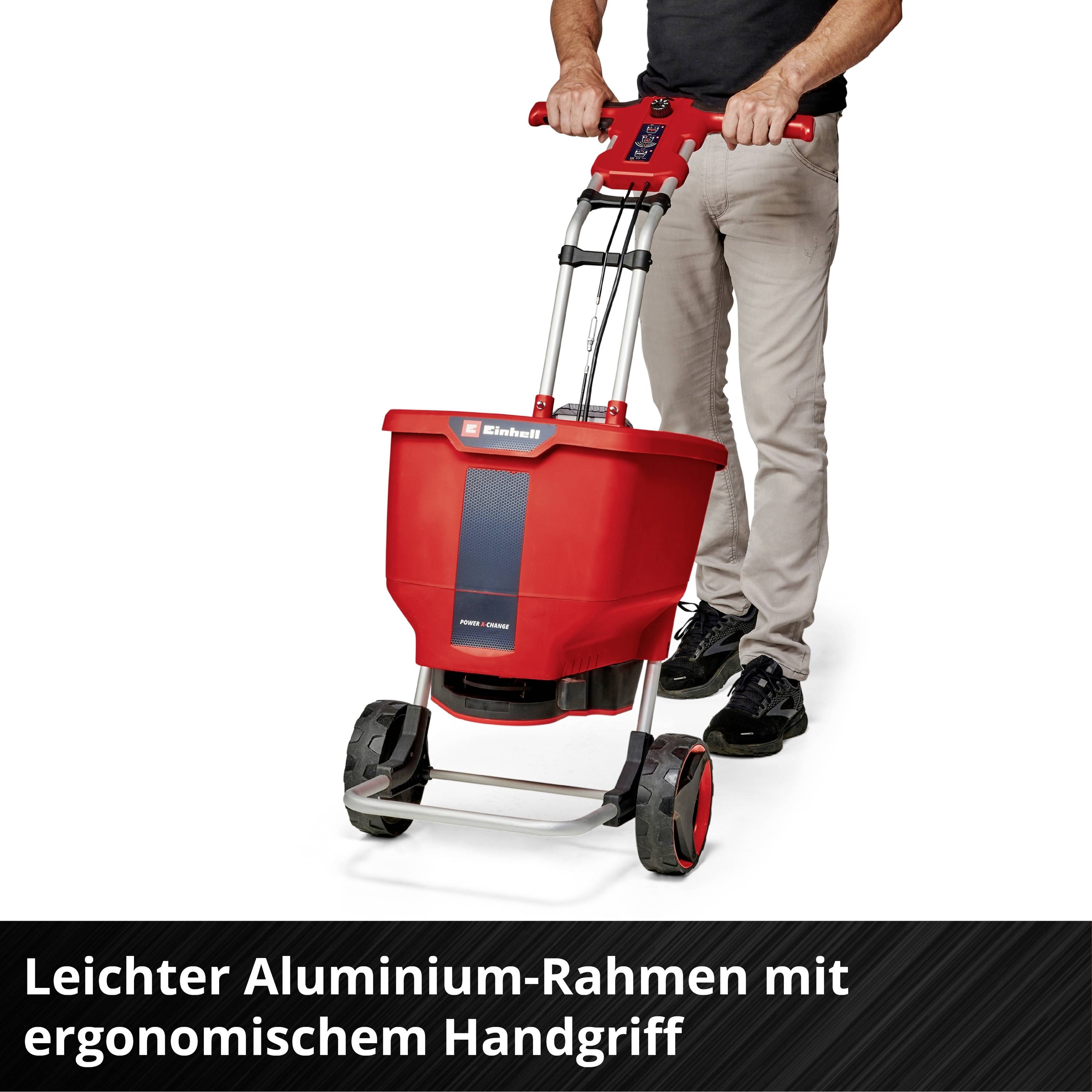Homme avec un chariot de dispersion rouge sur roues, 'Châssis léger en aluminium avec poignée ergonomique' en bas de l'image.