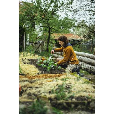 Une personne portant une veste marron plante des fleurs dans un jardin, entourée d'arbres et de clôtures en bois.