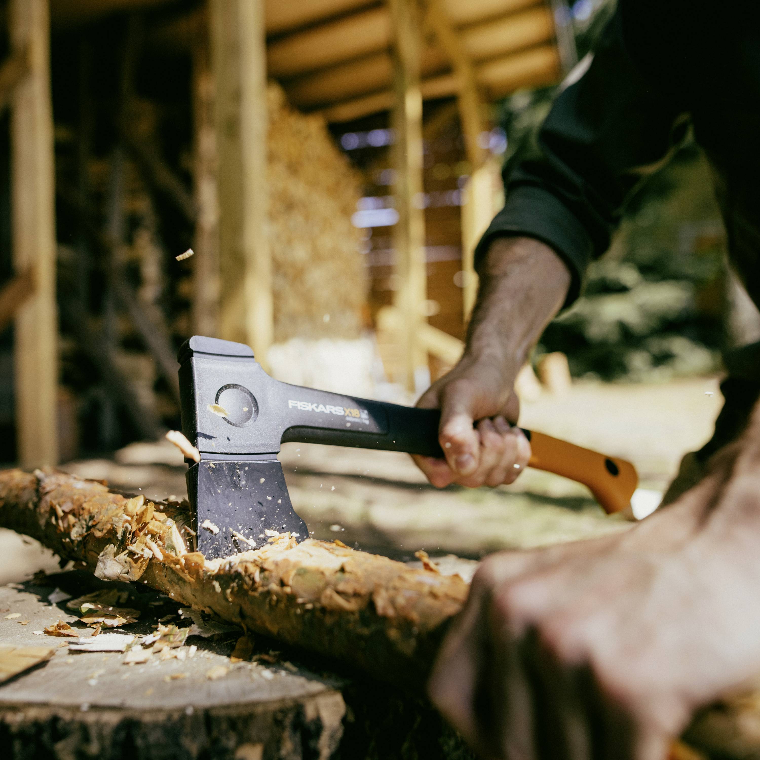 Une personne coupe un tronc d'arbre avec une hache à l'extérieur. Des copeaux de bois volent, l'environnement est rural.