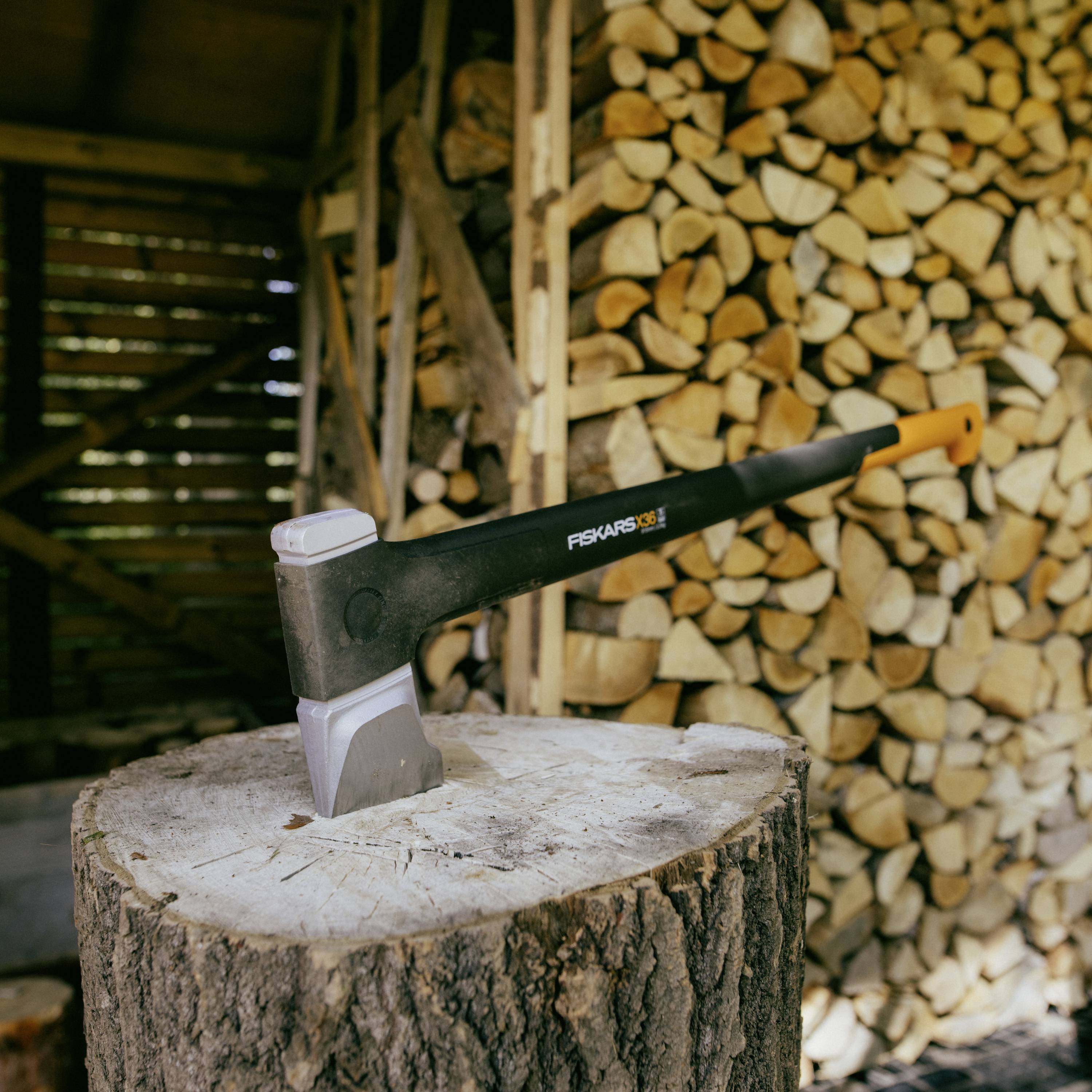 Une hache est plantée dans une souche de bois devant une pile de bois de chauffage coupé dans une cabane en bois.